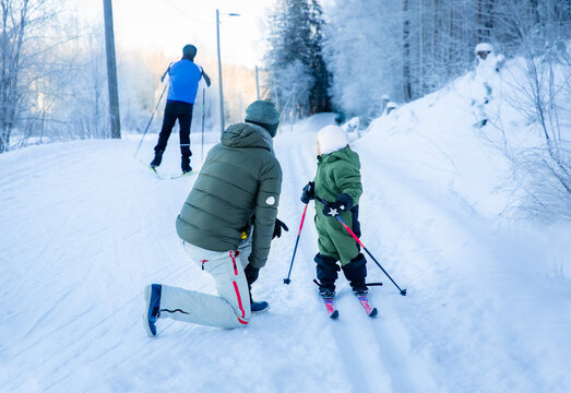 A father helps his toddler learn cross-country skiing on a snowy trail in Helsinki region, Finland, during an active winter family outing.