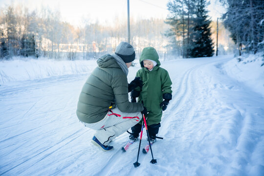 A father helps his toddler learn cross-country skiing on a snowy trail in Helsinki region, Finland, during an active winter family outing.