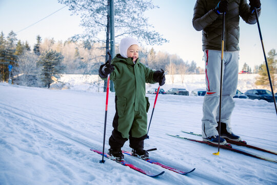 A father helps his toddler learn cross-country skiing on a snowy trail in Helsinki region, Finland, during an active winter family outing.