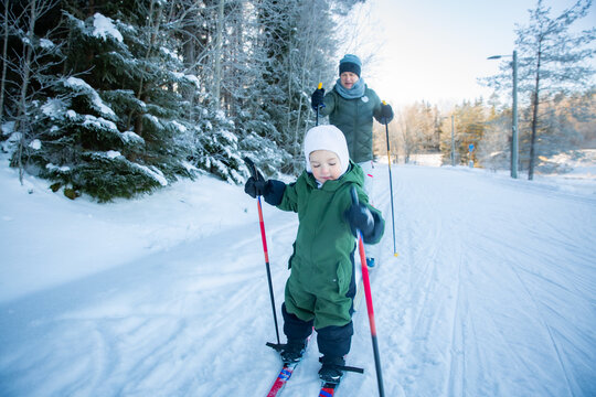 A father helps his toddler learn cross-country skiing on a snowy trail in Helsinki region, Finland, during an active winter family outing.