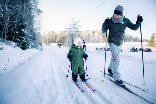 A father helps his toddler learn cross-country skiing on a snowy trail in Helsinki region, Finland, during an active winter family outing.