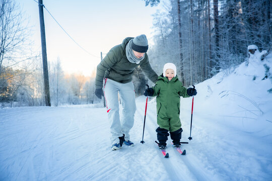 A father helps his toddler learn cross-country skiing on a snowy trail in Helsinki region, Finland, during an active winter family outing.