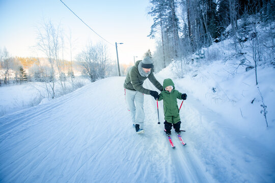 A father helps his toddler learn cross-country skiing on a snowy trail in Helsinki region, Finland, during an active winter family outing.