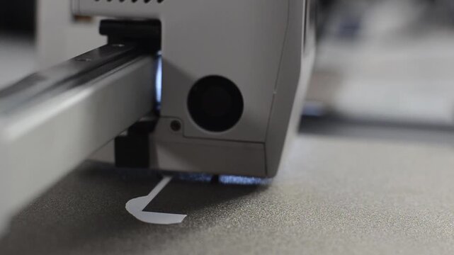 Macro shot of a 3D printer printhead extruding white plastic layer onto a heated bed