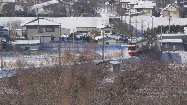 雪に覆われた冬の集落を走り抜ける長野電鉄の特急ゆけむり（1000形）
