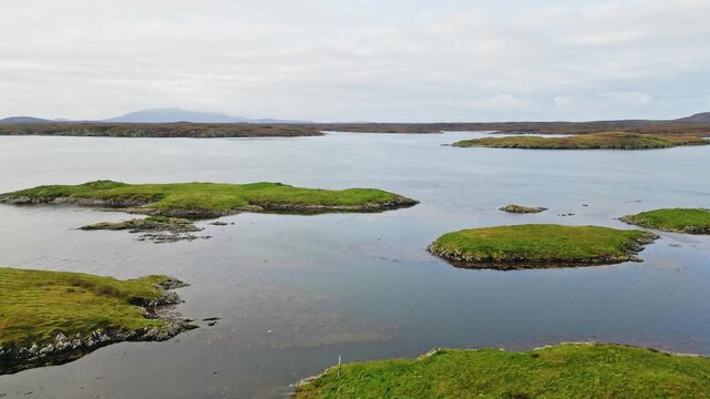 Coastal water and small grassy islets around Grimsay near North Uist in the Outer Hebrides, Scotland, showing an unspoiled remote island landscape, ascending aerial view