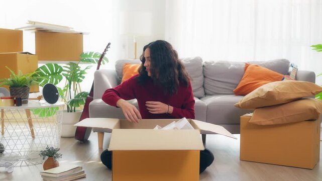 Young Hispanic woman arranging furniture and unpacking boxes in house.