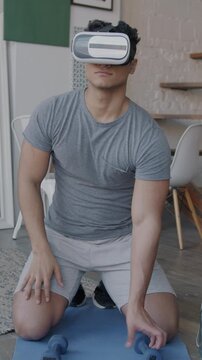 Young man wearing virtual reality glasses exercising with dumbbells doing sports indoors at home. Modern technology and active lifestyle concept.