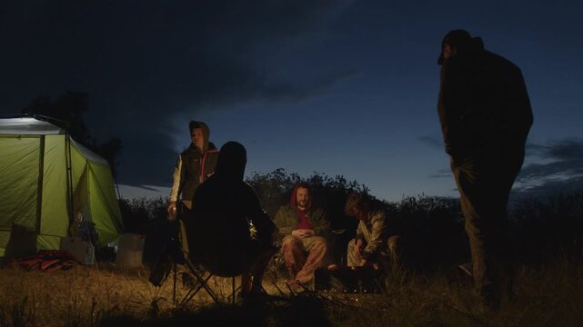 Group of men camping in the wild and gather near the bonfire and talk with each other. Fishermen camping and talk stories at night
