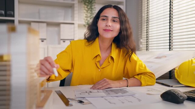 Young Hispanic woman architect sitting at desk, working in an office.