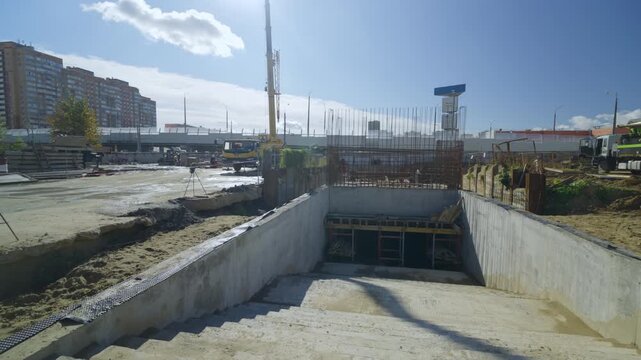 Concrete stairs lead into underground passage at active construction site. Bright sunlight illuminates urban modern development project