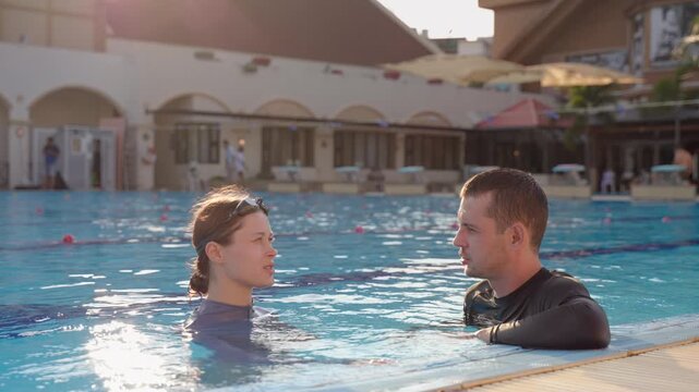 Athletic man and woman talking together in an outdoor swimming pool. 