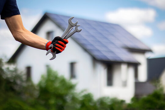 Solar Panels Installer. Hand of Solar Technician holding tools on Solar Panels House Background with Solar Panel Installation, Renewable Energy and Home Energy Efficiency.