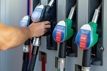 Person Selecting Fuel Pump Nozzle at Gas Station. Person reaching for a fuel pump nozzle beside several gasoline dispensers at a service station. © Iryna