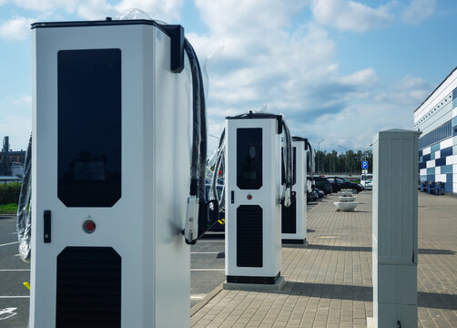 Modern electric vehicle charging stations standing in row at public parking lot under cloudy sky