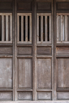 Weathered wooden panel door with vertical slatted windows, showcasing rustic texture and traditional architectural detail; suitable for backgrounds, heritage, interior design, restoration, and history
