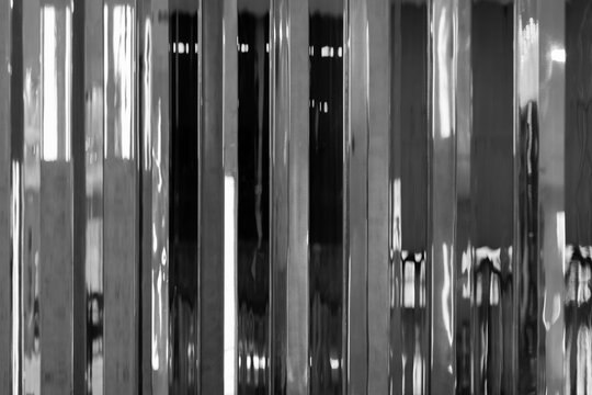 High-contrast black and white image of reflective metal panels creating vertical striped reflections and distorted mirrored patterns. Minimal, industrial composition with texture of strong lines 