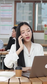 Asian Businesswoman Answering Phone Call While Working on Laptop