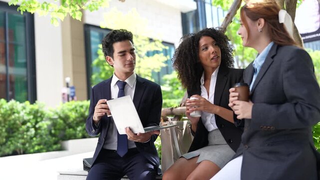 Businessman holds an open laptop while a Black businesswoman reads over it, an impromptu two-person work session in the open air of a modern Bangkok city office campus