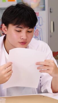 Teenage Student in Lab Coat Reading Scientific Paper in Classroom