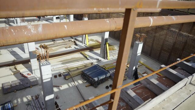 Concrete pillars stand in excavation pit under steel supports. Industrial building materials emphasize ongoing foundation layer development