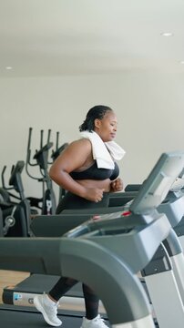 African American plus-size woman running on treadmill in fitness gym. 
