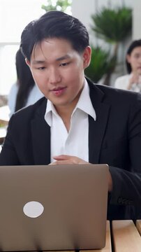 Asian Businessman in Black Suit Working on Laptop in Modern Office