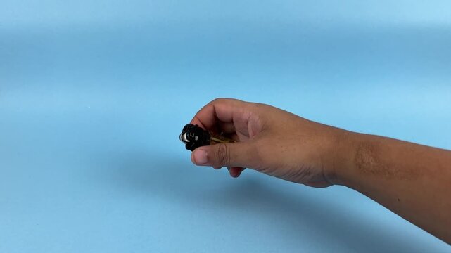 Hand Holding Lighter with Flame on Blue Background Close Up