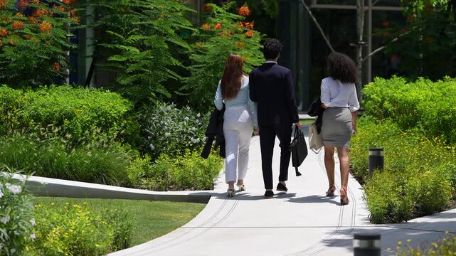 Three colleagues seen from behind as they walk deeper into a green office garden, an unobtrusive back view that suits corporate, ESG and recruitment voiceovers and captions
