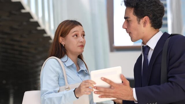 Tight two-shot of a businesswoman and a colleague going through a tablet outdoors, her question and his answer playing out in close-up against a soft and bright wall