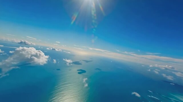 Aerial view gliding above turquoise ocean waters and scattered white clouds beneath bright sunlight, expansive blue horizon and atmospheric seascape filmed from high altitude