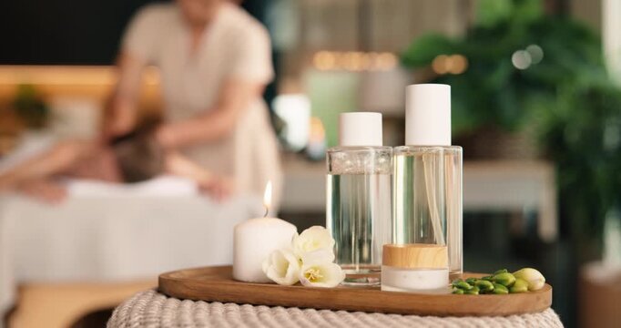Oil, cream and candle in spa for massage, aromatherapy and client with pamper treatment by masseuse. People, container and fragrance product in beauty salon for wellness, moisturizer and self care.