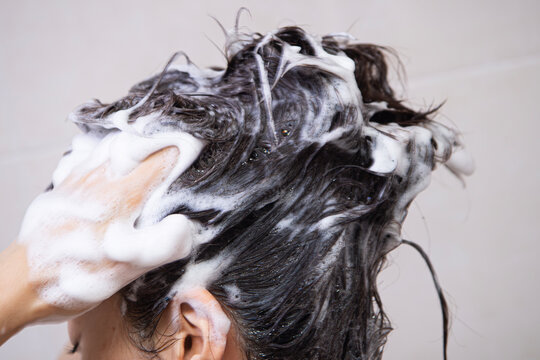 Woman washing hair with shampoo foam close up
