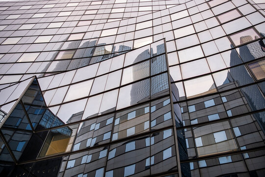 Angular glass facade with reflective windows and geometric projections on a contemporary building, creating an abstract pattern of lines and urban architecture.