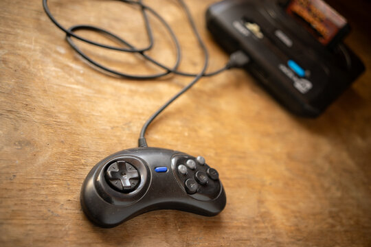 A wired game controller on a wooden table next to the second gamepad. Video games and interactive entertainment. Multiplayer games and home entertainment.A game console from the 90s.