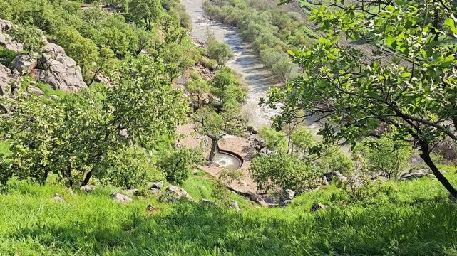 Sweeping green valley view with a bubbling spring beside a winding river through lush hills and farmland, toward distant mountains with patches of snow and clouds.
📍Ghol spring, Sarvabad, Kurdistan 