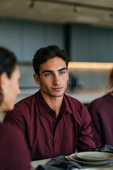 Fototapeta premium Young man facing camera at dining table in burgundy shirt for lifestyle portrait background and social gathering banner
