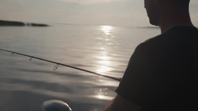 Amateur angler fishing on the river from a boat at sunset