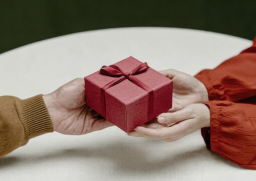 Hands exchanging a gift wrapped in red paper with a bow on a white round table
