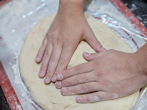 Hands pressing dough for baking on a work surface covered