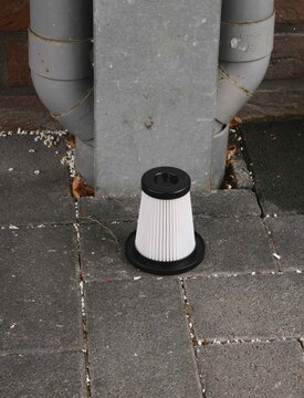 Water filter left on pavement next to pipes outside a building on a cloudy day
