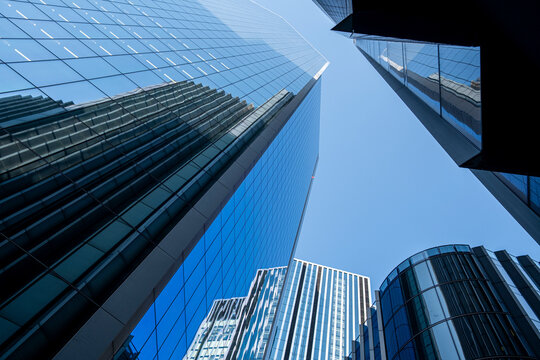 Upward view of modern office towers in the City of London, framed by blue glass facades and converging lines in the financial district.