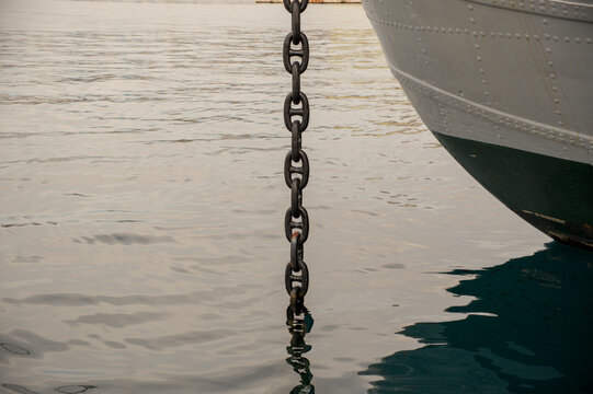 Heavy steel anchor chain extending into the sea beside a ship hull in Rijeka harbor, Croatia. Vessel anchoring system detail.