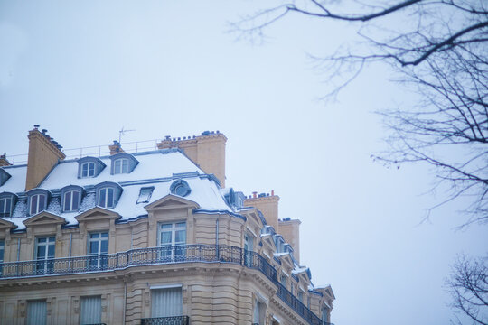 Snow-covered Parisian apartment building with mansard roof, dormer windows, balconies and classic Haussmann-style facade