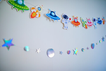 Space-themed birthday decorations on a wall with colorful paper astronauts, rockets, UFOs, stars and planets garlands © Ekaterina Pokrovsky