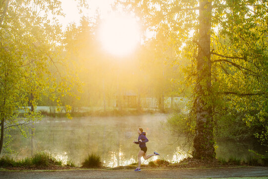 White runner jogging on trail in park at misty morning sunrise
