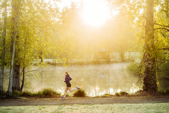 White runner jogging in morning park with sunlight and mist