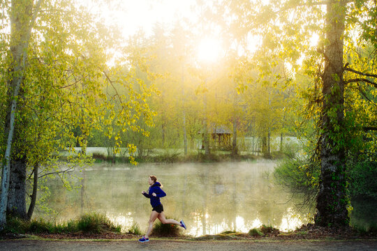 White runner jogging in misty park by lake at sunrise