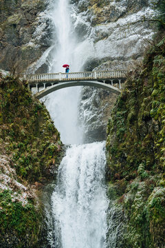 White person with umbrella standing on bridge over multnomah falls