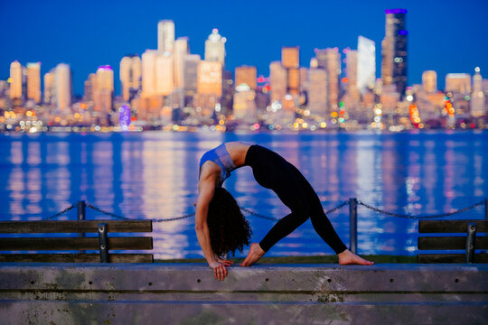 White woman doing yoga backbend by Seattle waterfront at evening